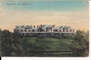 Une carte postale en couleur montrant un grand bâtiment rouge en trois parties avec un toit vert. Il s’agit du Hackmatack Inn qui se trouve au somment d’une colline avec vue sur le Black Harbour à Chester. Deux parties de la façade du bâtiment ont une véranda. On peut voir les terrains de tennis au premier plan. Le Hackmatack Inn était l’un des grands hôtels dont l’eau venait de Hawboldt Gas Engines. Son promoteur, M. Keasby, était l’un des premiers investisseurs du projet