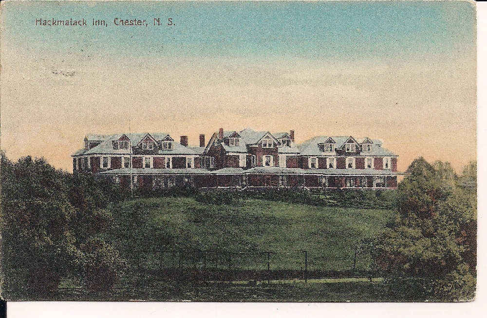 Une carte postale en couleur montrant un grand bâtiment rouge en trois parties avec un toit vert. Il s’agit du Hackmatack Inn qui se trouve au somment d’une colline avec vue sur le Black Harbour à Chester. Deux parties de la façade du bâtiment ont une véranda. On peut voir les terrains de tennis au premier plan. Le Hackmatack Inn était l’un des grands hôtels dont l’eau venait de Hawboldt Gas Engines. Son promoteur, M. Keasby, était l’un des premiers investisseurs du projet.