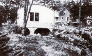 A black and white photo showing the rounded roof of the generating station on the East River, with the river running from under the station. On the right of the generating station, a small house which was where the operator of the generating station lived with his family.