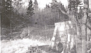 A black and white photo showing the water rushing over the Chester Electric dam on the East River. The dam, constructed of concrete has the date 1919 on it.