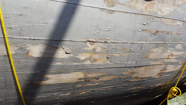 Color photograph showing the detail of the hull of a gray-painted wooden boat, whose paint is peeling.