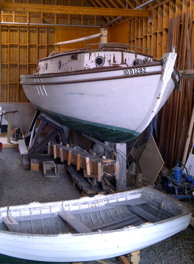 Color photograph of a white, brown and green wooden boat on a trestle inside a building.