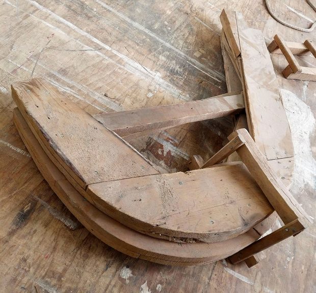 Current photograph of a U shaped wooden template, in close-up, placed on a workbench.