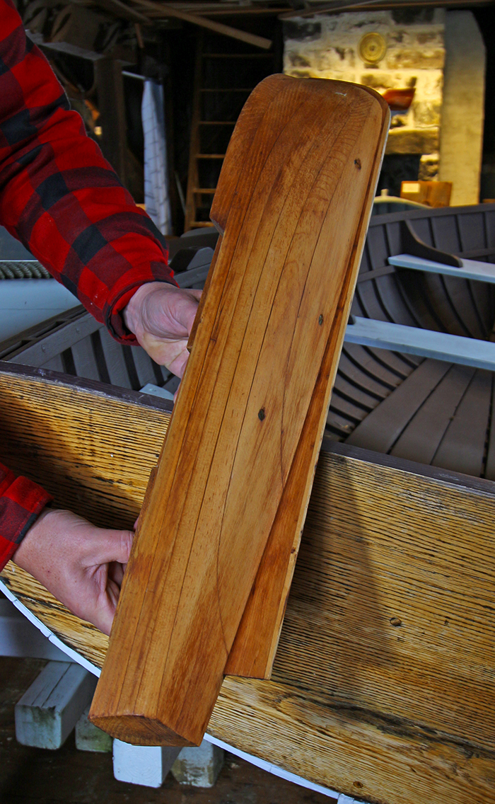 Color photograph of a wooden half hull, presented vertically, whose profile and underside are visible.