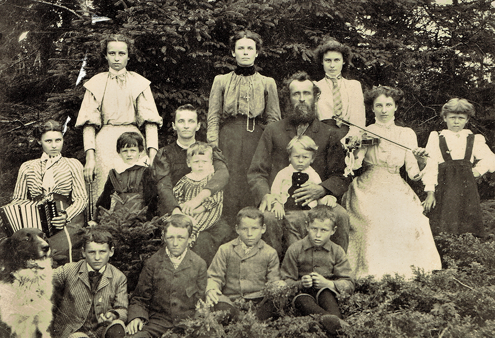 Black and white photograph showing the parents of François-Xavier Lachance, their 13 children and their dog. All look at the camera, sitting or standing in front of a woodlot.