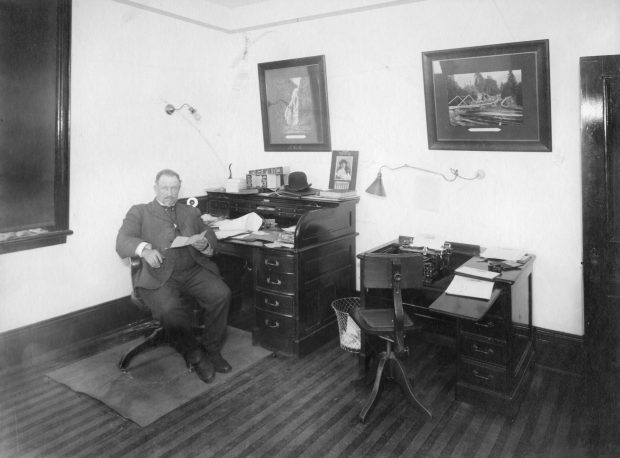 Man in a suit sitting at a desk in a small office.