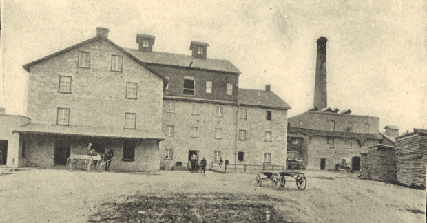 Four storey stone mill with employees and carriages in the front.