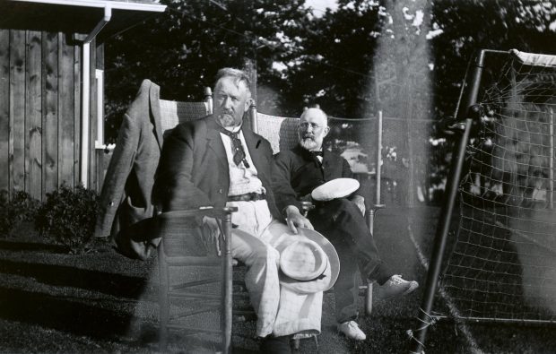 Two men sitting on chair by a tennis net.