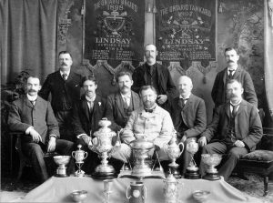 Nine men sitting with trophies and championship banners.