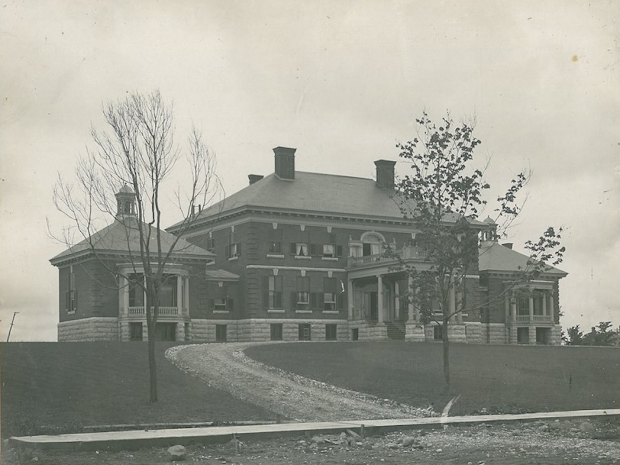 Brick building atop a hill with a dirt driveway leading to it.