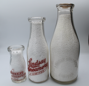 Three different sized milk bottles that are either embossed or have applied colour labels