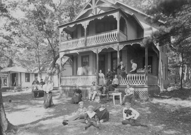 Adults and children outside of a two storey frame cottage.