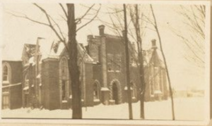 Brick building with a fence and trees lining the entrance.