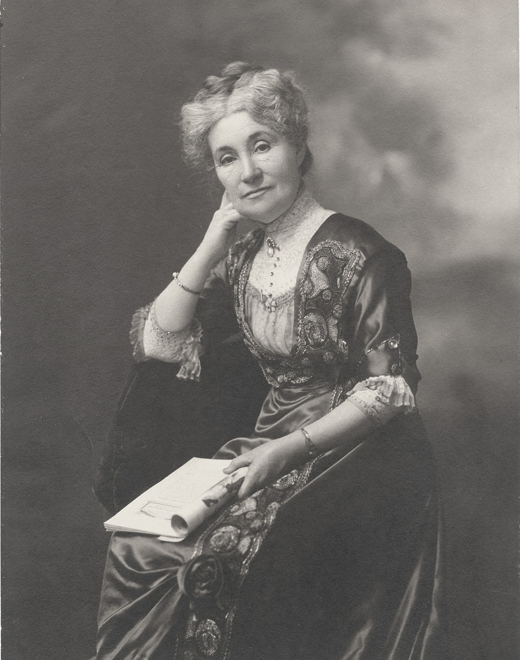 Woman with grey hair wearing a black dress with a book in her hand.