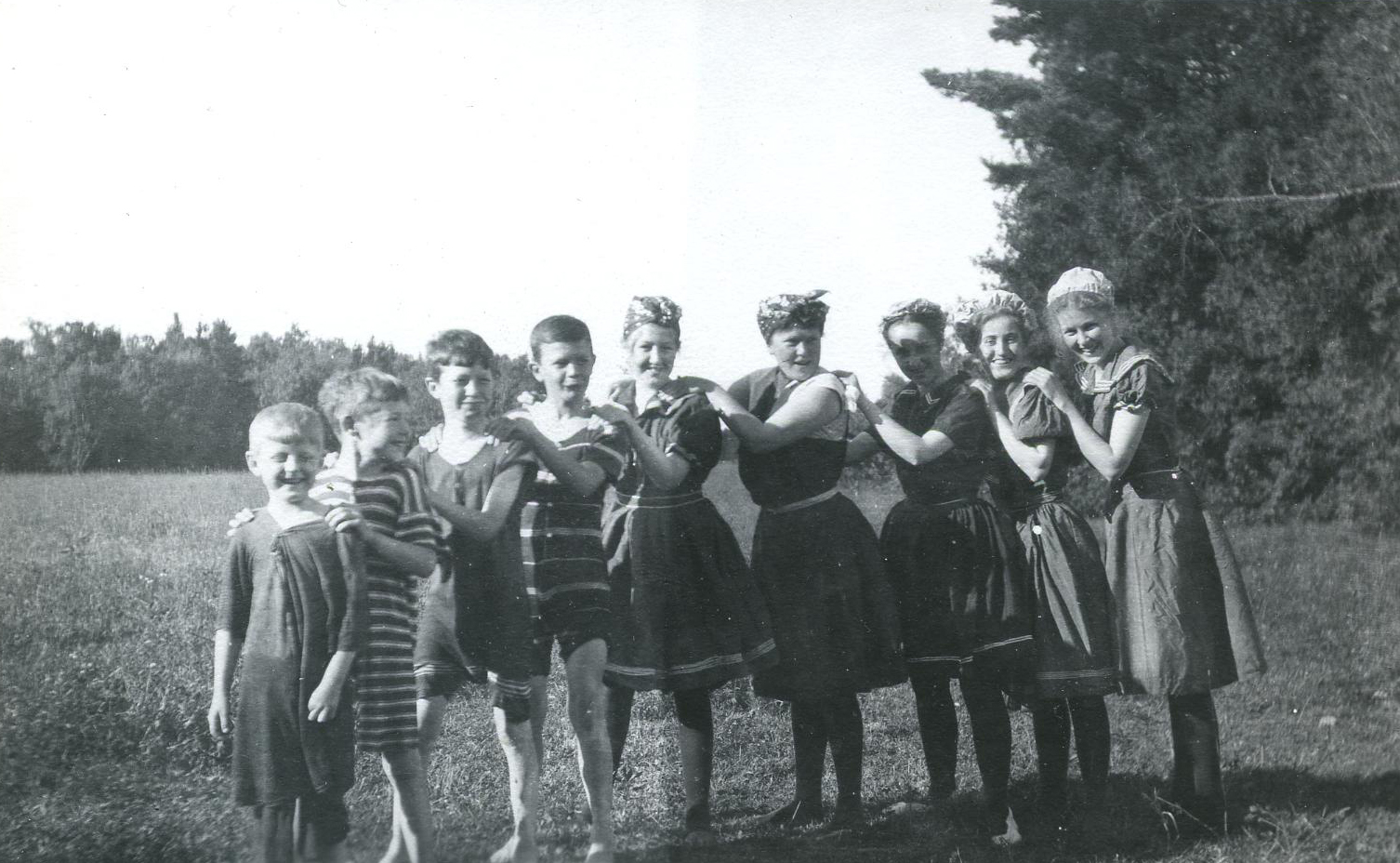 Nine children standing on grass beside each other wearing their bathing suits.