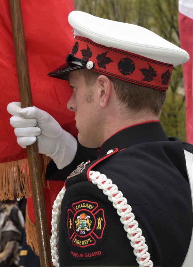 Close up of flag bearer from left shoulder patch to white cap, in ¾ profile, showing white gloved right hand holding flag pole upright.