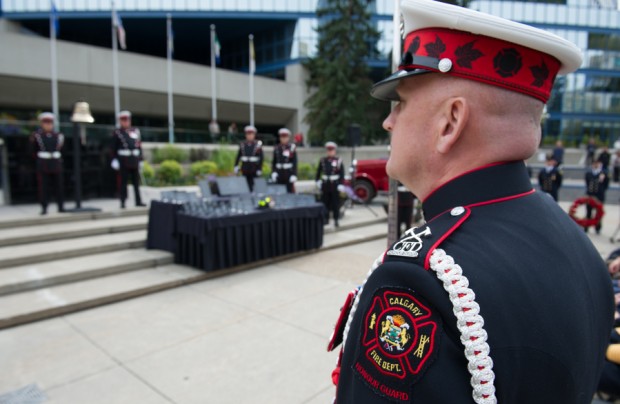 Uniformed Commander is seen in 3/4 profile from behind, from waist up, in full uniform. In background is Tribute Plaza and City Hall.