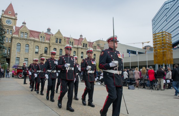 Honour Guard marches in full dress uniform at Tribute Plaza in front of old city hall, holding ceremonial swords and axes.