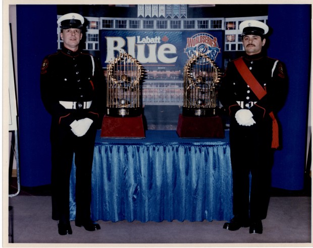 Guard Members Rick Choppe and Shannon Pennington stand with the 1993 World Series baseball trophies, both in full dress. The trophies are displayed on a table draped in a blue cloth, with blue background.