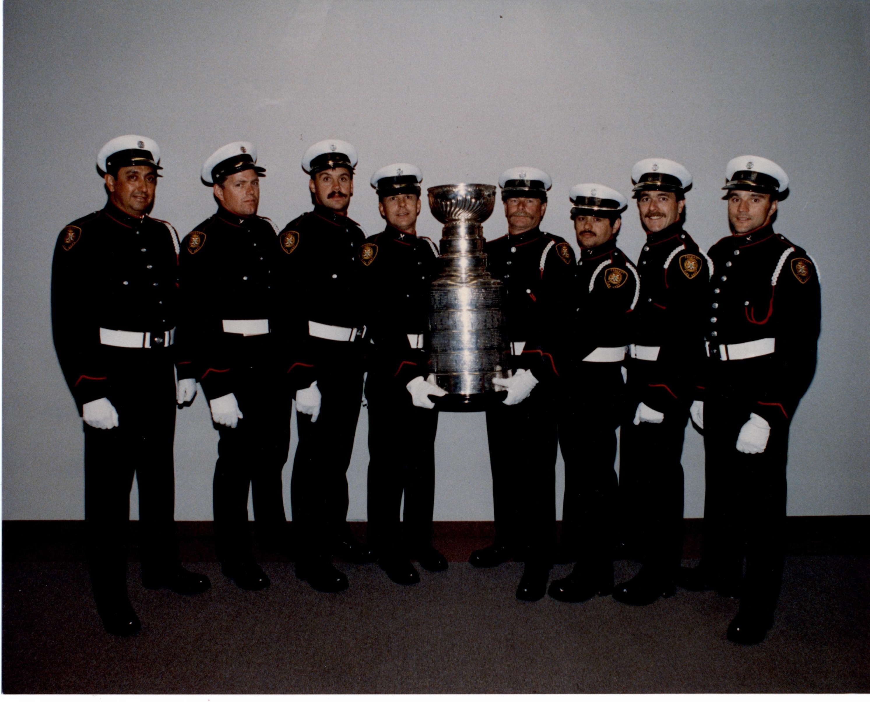 Eight firefighters in uniform stand either side of the Stanley Cup, being held up in centre.