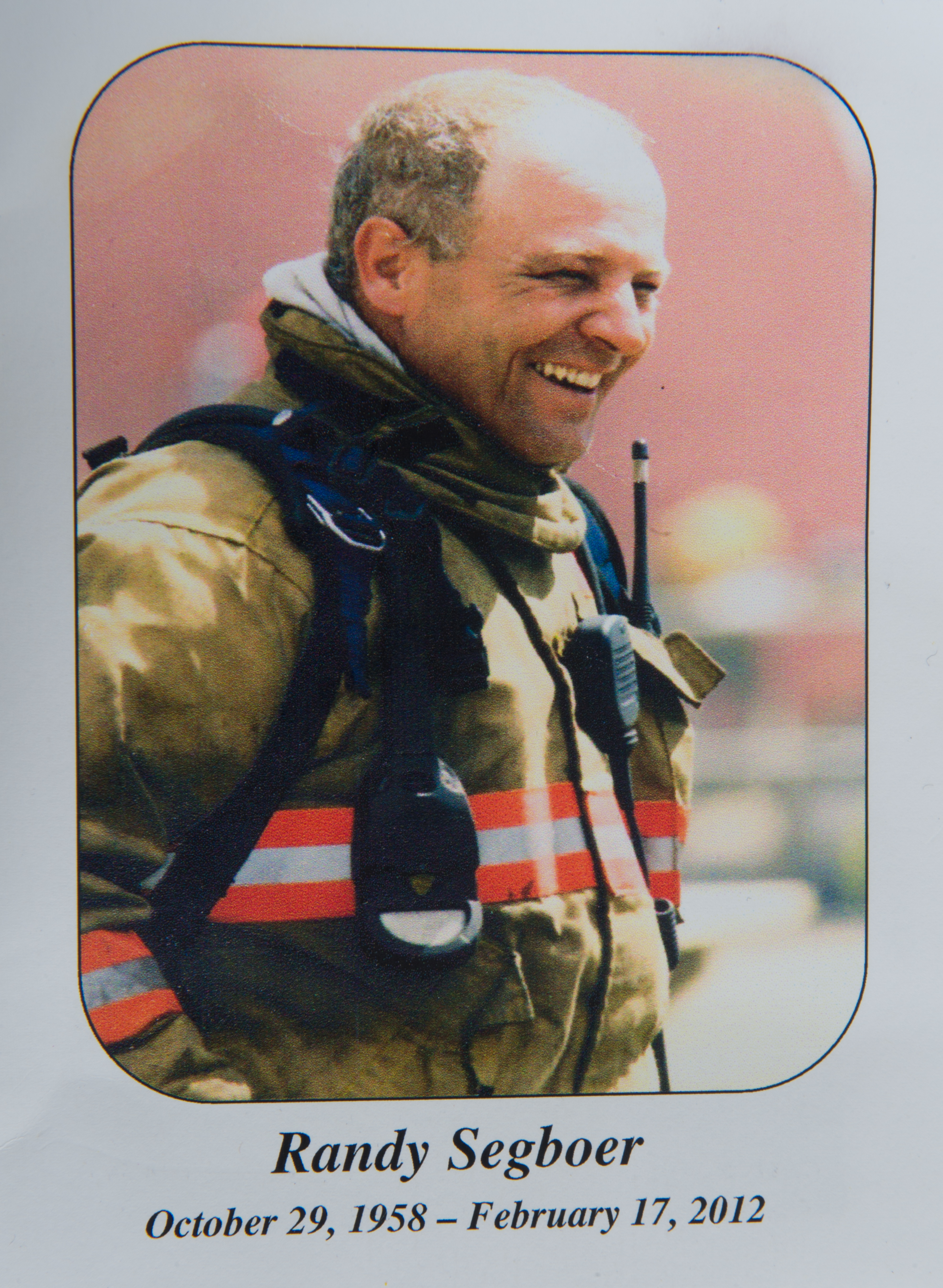 Memorial photo card showing a smiling firefighter in firefighting gear. Underneath the photo is: 'Randy Segboer October 29, 1958 - February 17, 2012'