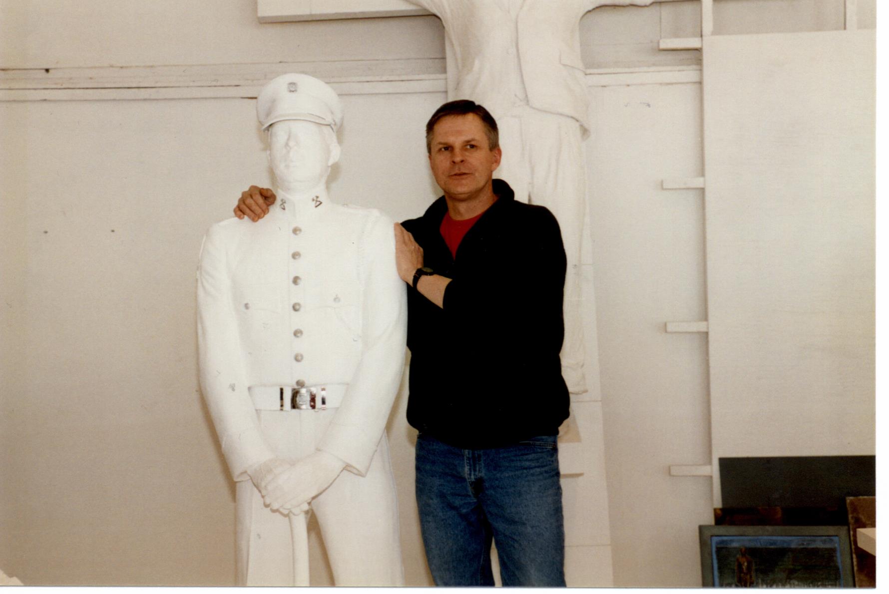 Member Rick Choppe, in casual clothes, stands next to his life size white plaster cast, in uniform, for the honour guard statue.