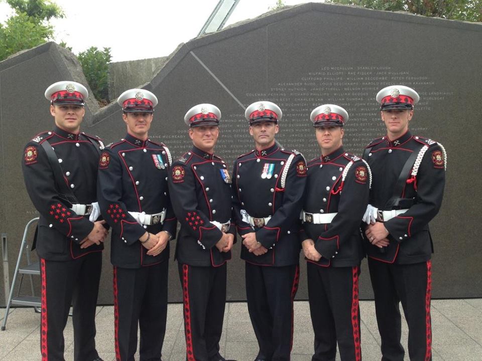 Six Honour Guard members stand with hands together in front of the engraved memorial in Ottawa.