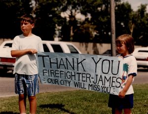 Along the route of the procession two children hold up a banner: 'Thank You Firefighter James. Our City will miss you.'
