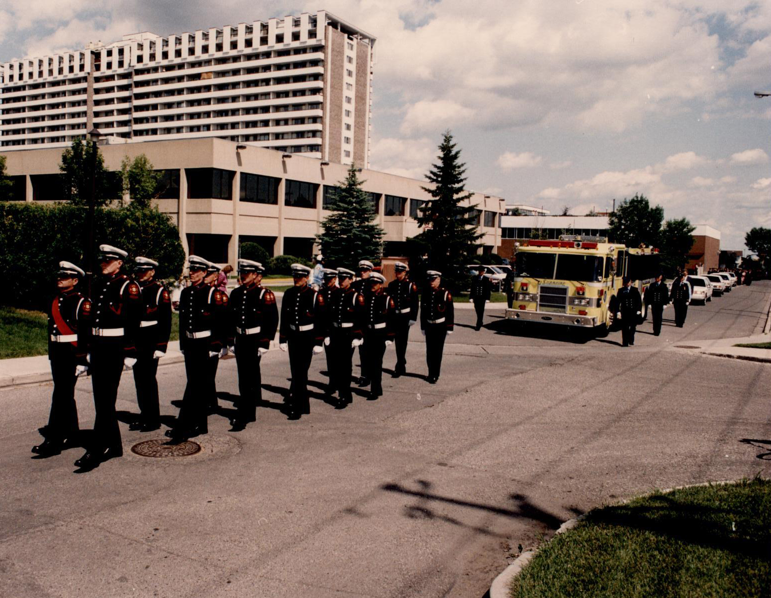 Several Honour Guard members march in full dress, leading a yellow fire engine at the front of Morley James' funeral procession.