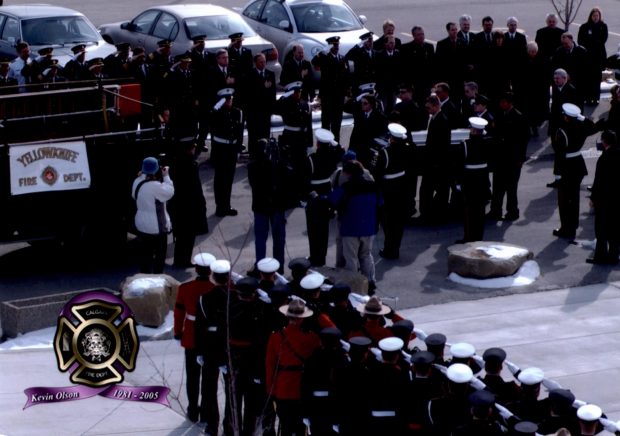 CFD Honour Guard load the casket of Kevin Olson, a Yellowknife firefighter, onto the ceremonial pumper with Olson's casket, while unformed firefighters and Mounties stand to attention and salute.