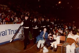 Honour Guard marching through the crowd seated on bleachers and on floor seats at a community parade.