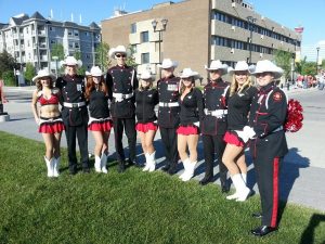 Five uniformed Guard members are pictured with five Stampeders' Outriders in their cheerleading uniforms and white hats