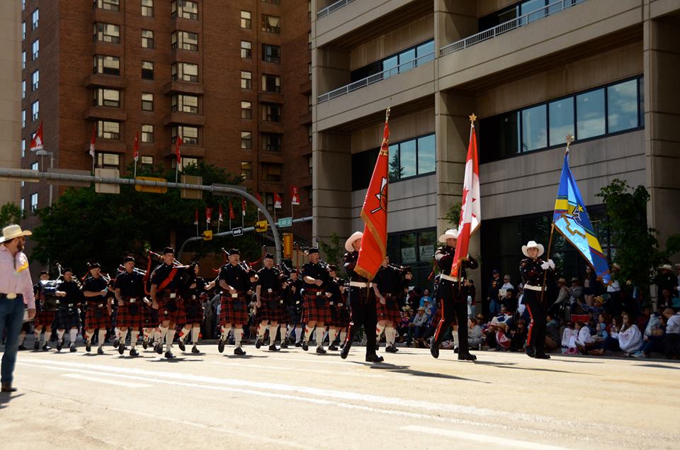 Honour Guard parades through downtown with departmental, national and union flags at 2015 Stampede, followed by the red kilted Pipes and Drums.