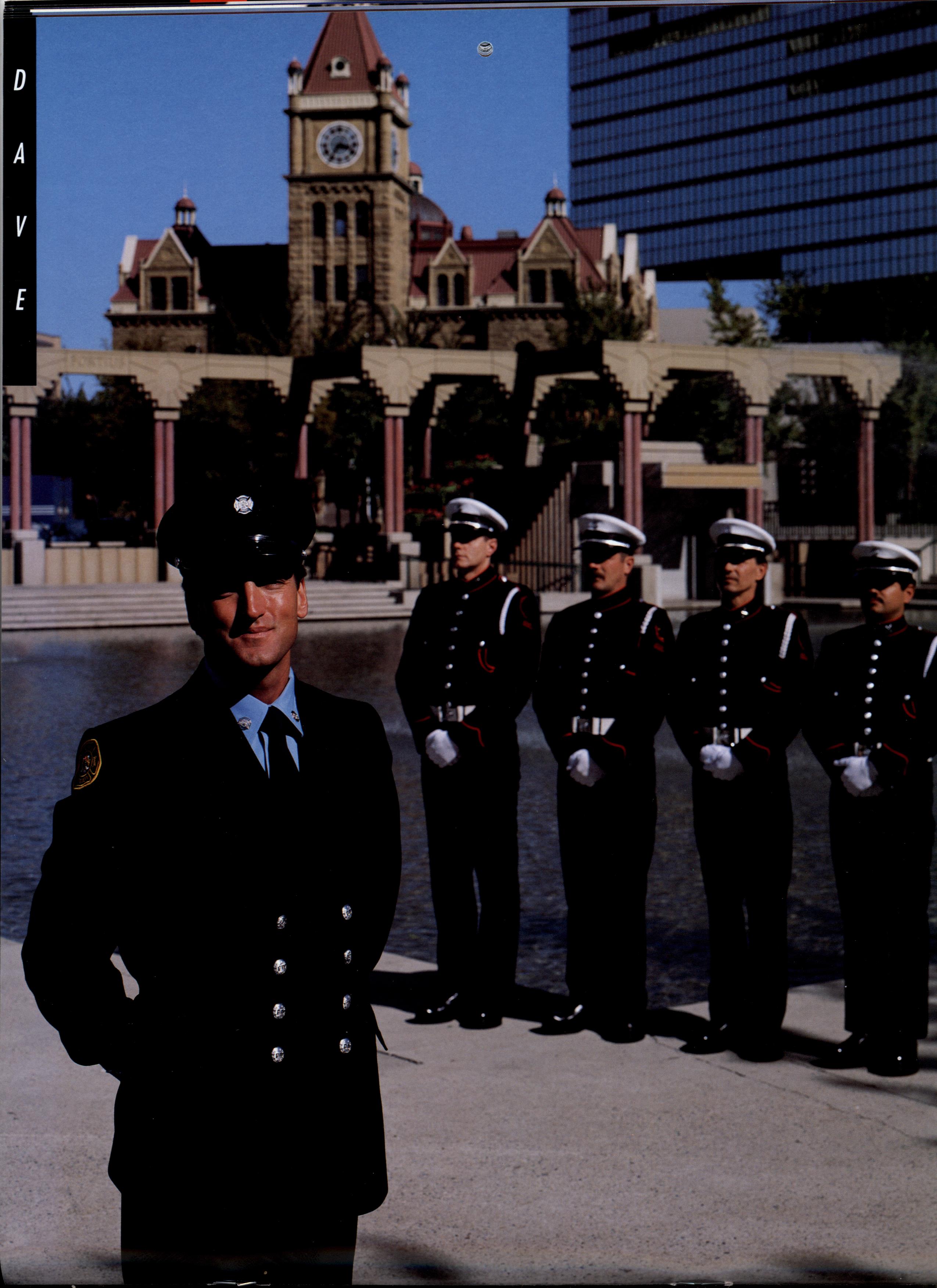 A firefighter stands in the left foreground, with four Honour Guard members standing at attention mid ground. In the background is Olympic Plaza and historic sandstone city hall.