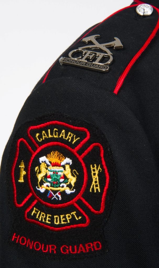 Gros plan de l’épaule droite de la veste de la garde d’honneur avec insigne et logo du service d’incendie de Calgary et épinglette argentée aux haches croisées de la garde d’honneur