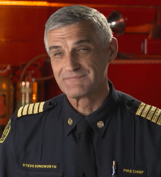 Colour photograph of Chief Steve Dongworth smiling in black uniform with gold accents representing his rank on his shoulders.