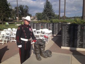 A CFD Honour Guard in unifrom with white belt, gloves and cowboy hat stands with a sculpture of boots, in front of a memorial wall inscribed with names.