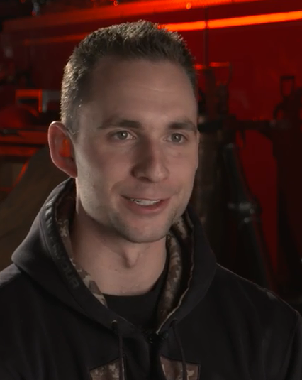 Head and shoulder colour photo of Steven Leschert wearing a dark jacket with a red back lit background.