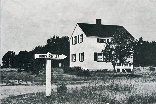 Black and white photograph of a white house and a sign pointing to Tomkinsville