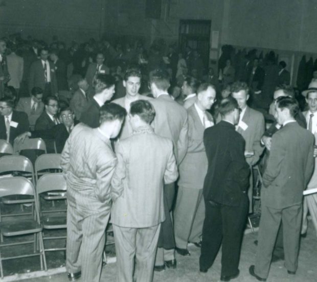 A large gathering of mostly men in suits standing and talking.
