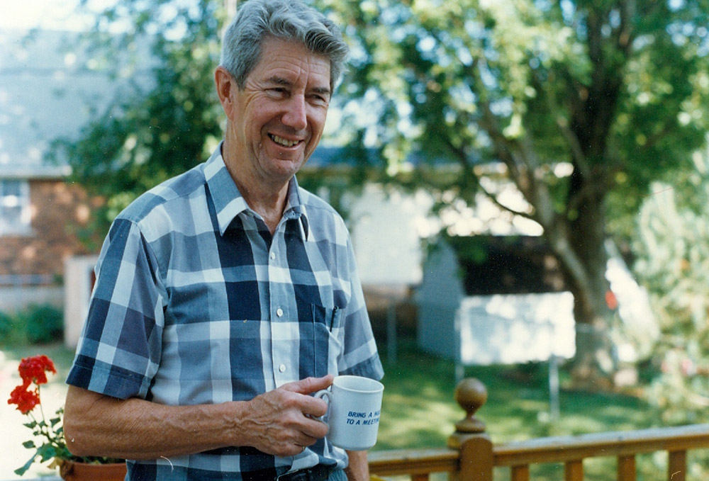 Colour photograph of a man in a blue plaid shirt with a mug in his hand