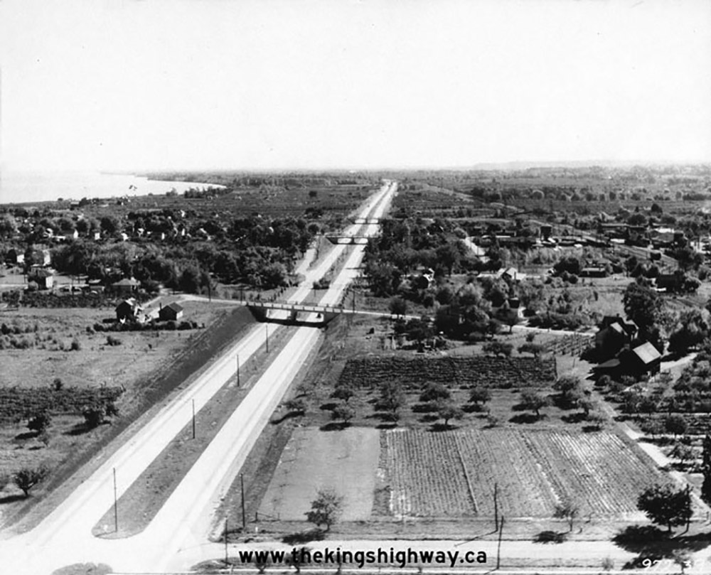 Black and white photo of Queen Elizabeth way facing East towards Grimsby area passing through a rural landscape with the lakeshore at the left.