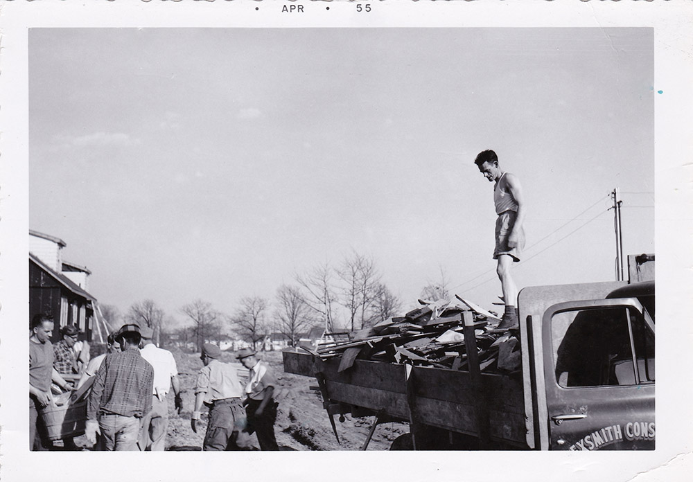 Black and white photograph of men unloading a truck. At the top is typed 