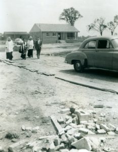 Black and white photograph of four men walking towards a car. Three Priests and a man in a suit