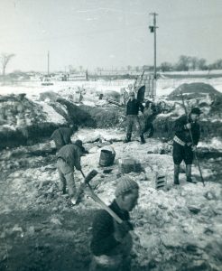 Photo noir et blanc d’un groupe d’hommes déblayant la neige sur un chantier de construction.