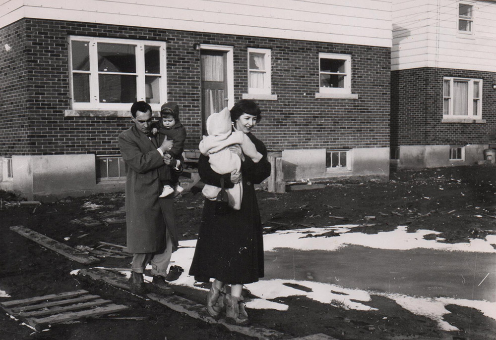 Black and white photograph of a family walking on boards over mud