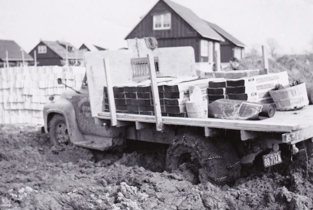 black and white photograph of a loaded truck with chains stuck in the mud