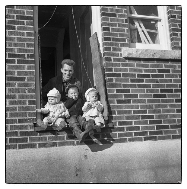 black and white photograph of a man and three children sitting in a door of a house under construction