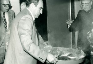 Black and white photograph of a man burning papers in a tray. Men around watching