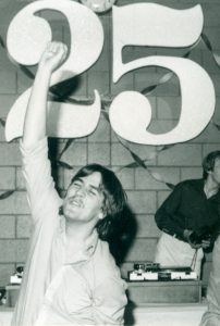 Photo noir et blanc d’un jeune adulte dansant devant la pancarte d’un gros numéro 25.
